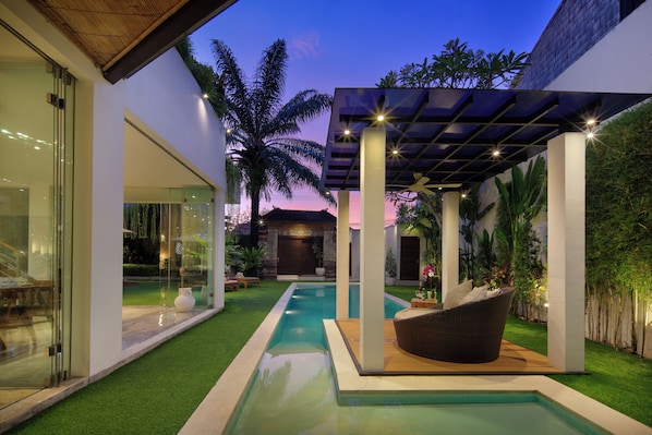 A modern outdoor pool area with a pergola, seating, and a view of the sky.