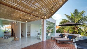 A modern outdoor deck with wooden flooring, a ceiling with natural light fixtures, and a view of a lush garden.