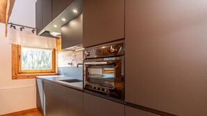 Een moderne keuken met roestvrijstalen apparatuur, een raam met uitzicht op bomen en een houten vloer.
