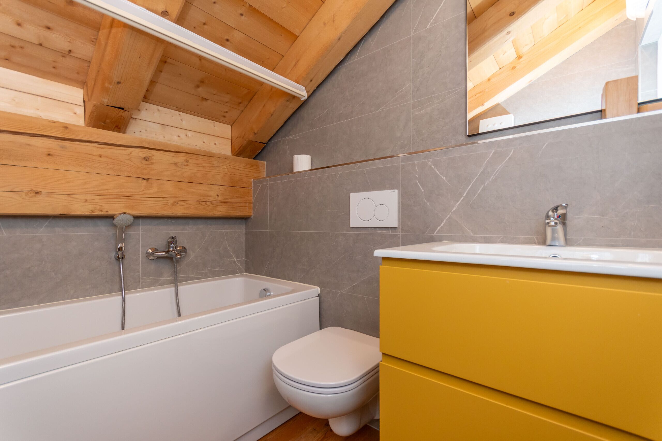 A bathroom with a bathtub, toilet, and yellow cabinets.
