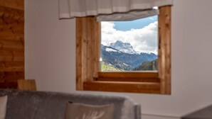 Een kamer met een raam met houten kader dat uitkijkt op een berglandschap.
