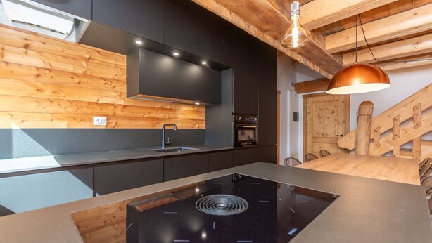 Een moderne keuken met een zwart inductiekookplaatje, houten wandpanelen en een houten trap.