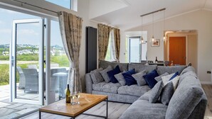 Ein modernes Wohnzimmer mit einem grauen Sofa, einem Holztisch und Blick ins Freie.