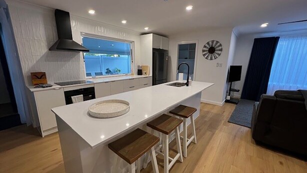 Een moderne keuken met een centraal eiland, barstoelen en een eethoek.