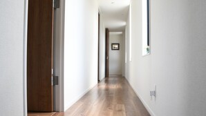 Un couloir au sol en bois et aux murs blancs, qui mène à une porte au fond.