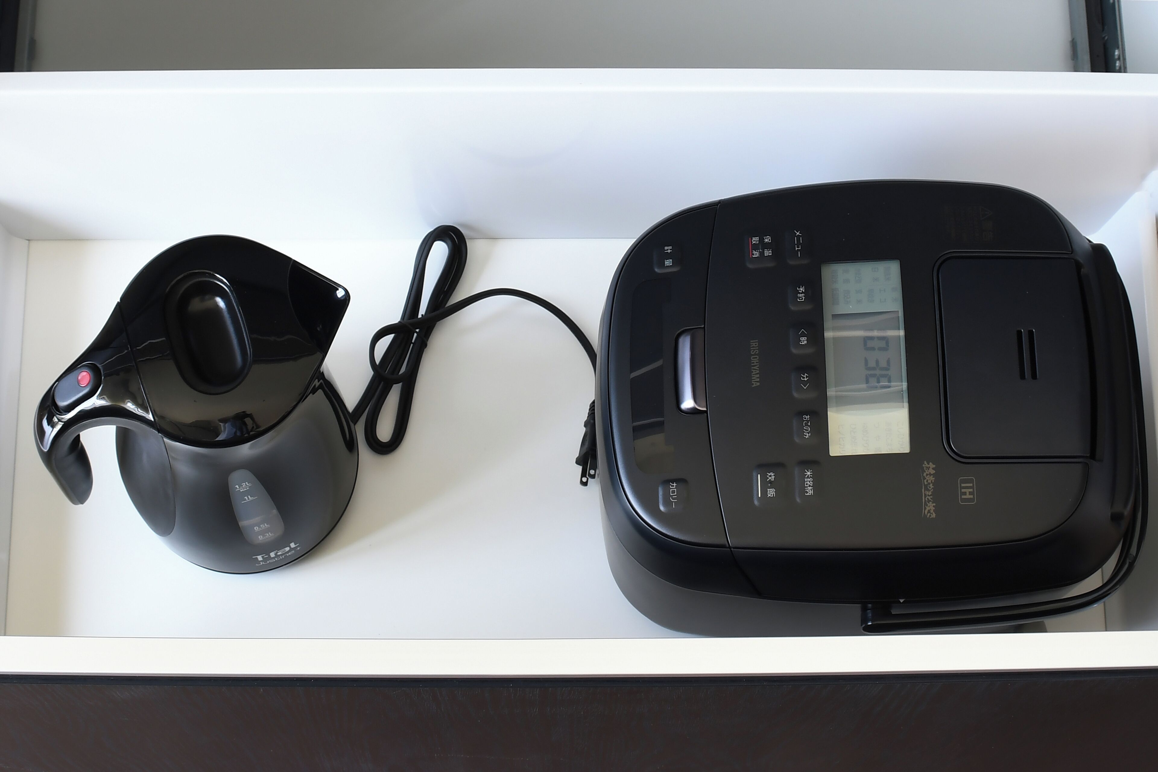 A white drawer containing a black electric kettle and a black portable heater.