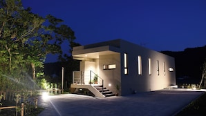 Une maison moderne à deux étages, dotée d’un toit plat, d’un escalier menant à l’étage supérieur et d’une entrée bien éclairée.