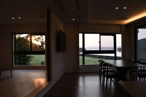 Amplia habitación con grandes ventanales que ofrecen vistas a un lago y montañas lejanas.