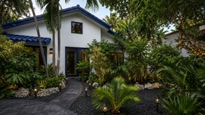 Una casa moderna con fachada blanca, techo azul y un camino que lleva a la entrada.