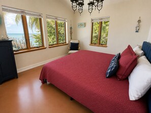 A bedroom with a large bed, multiple windows, a chair, and a dresser.