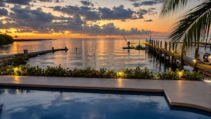 Una piscina con vista a un atardecer sobre el agua, un muelle y una palmera.