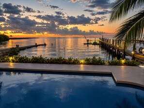 Una piscina con vista su un tramonto sull'acqua, un pontile e una palma.