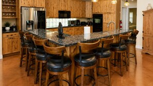 Cocina con gabinetes de madera, una isla central con taburetes de bar, electrodomésticos de acero inoxidable e iluminación colgante.