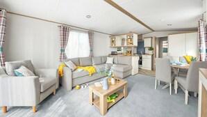 A modern living room with a sofa, coffee table, and dining area. - Platinum 3 No Pet Sleeps 6 (Penhallow)