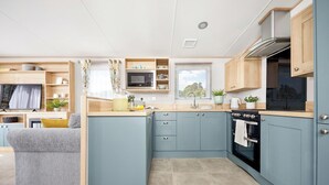 A compact kitchen with blue cabinets, a built-in oven, and a microwave. - Platinum 3 No Pet Sleeps 6 (Penhallow)