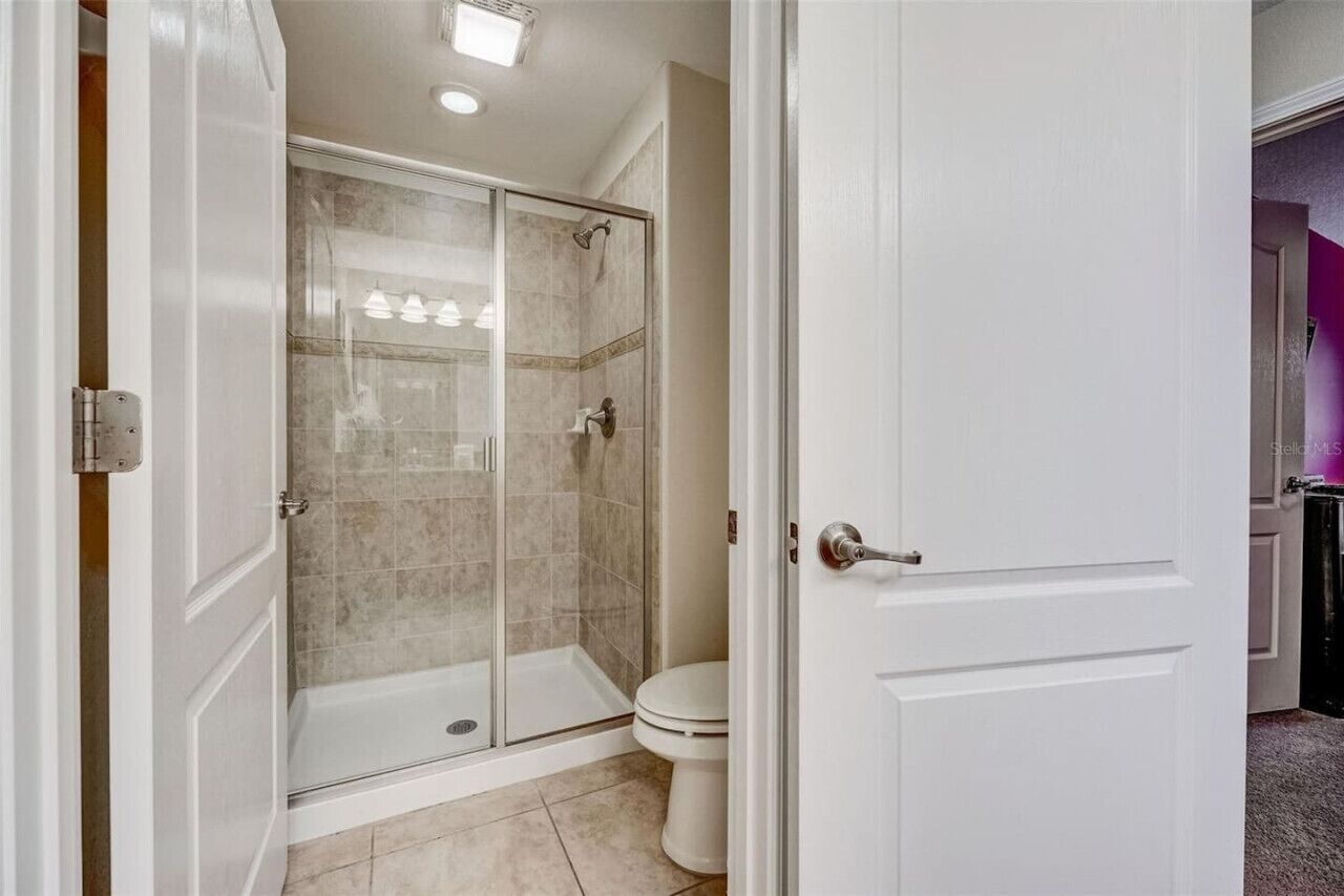 Een badkamer met een douchecabine van glas, een toilet en een witte deur.