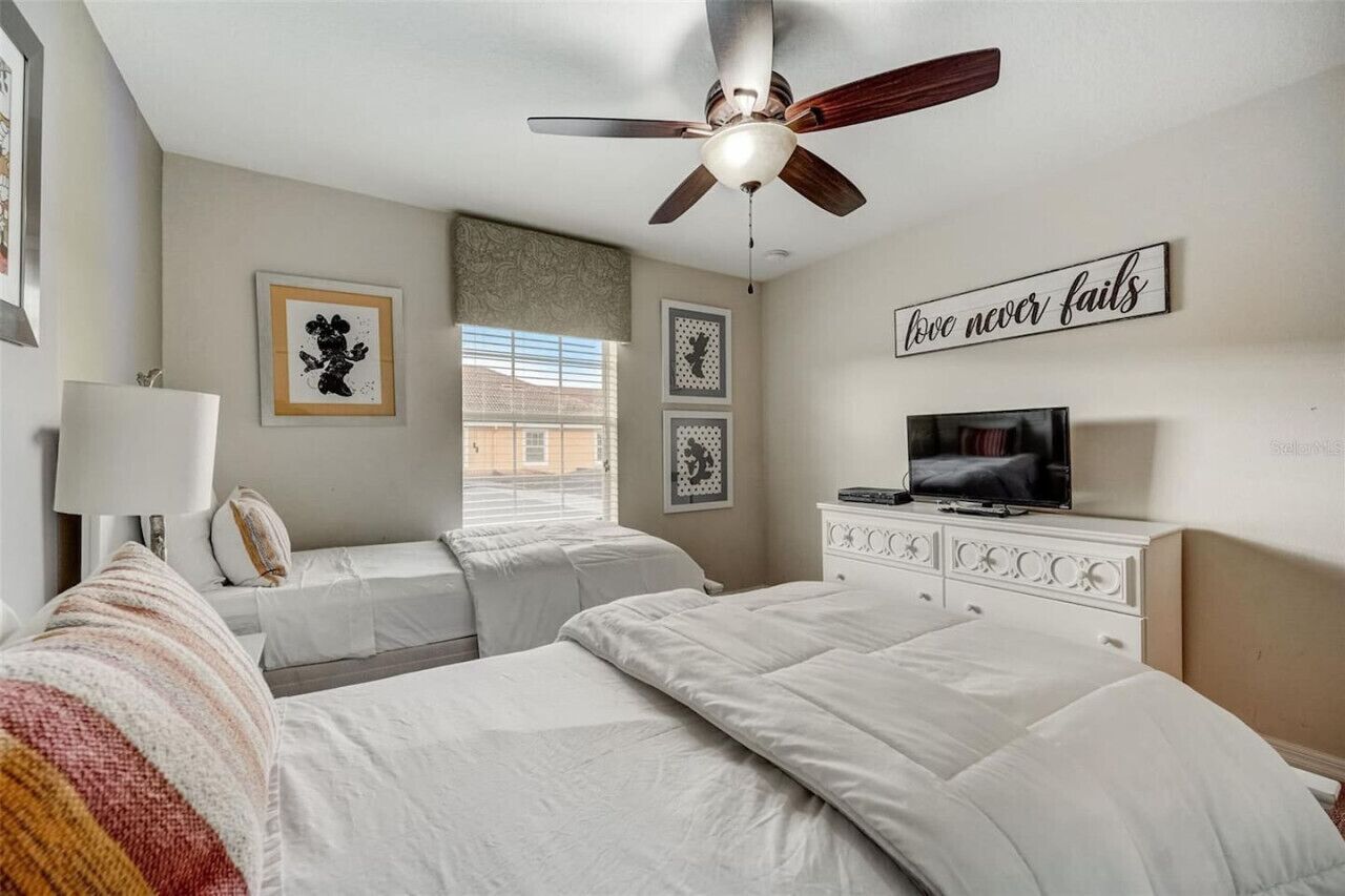 A bedroom with two beds, a ceiling fan, a TV, and a motivational quote on the wall.