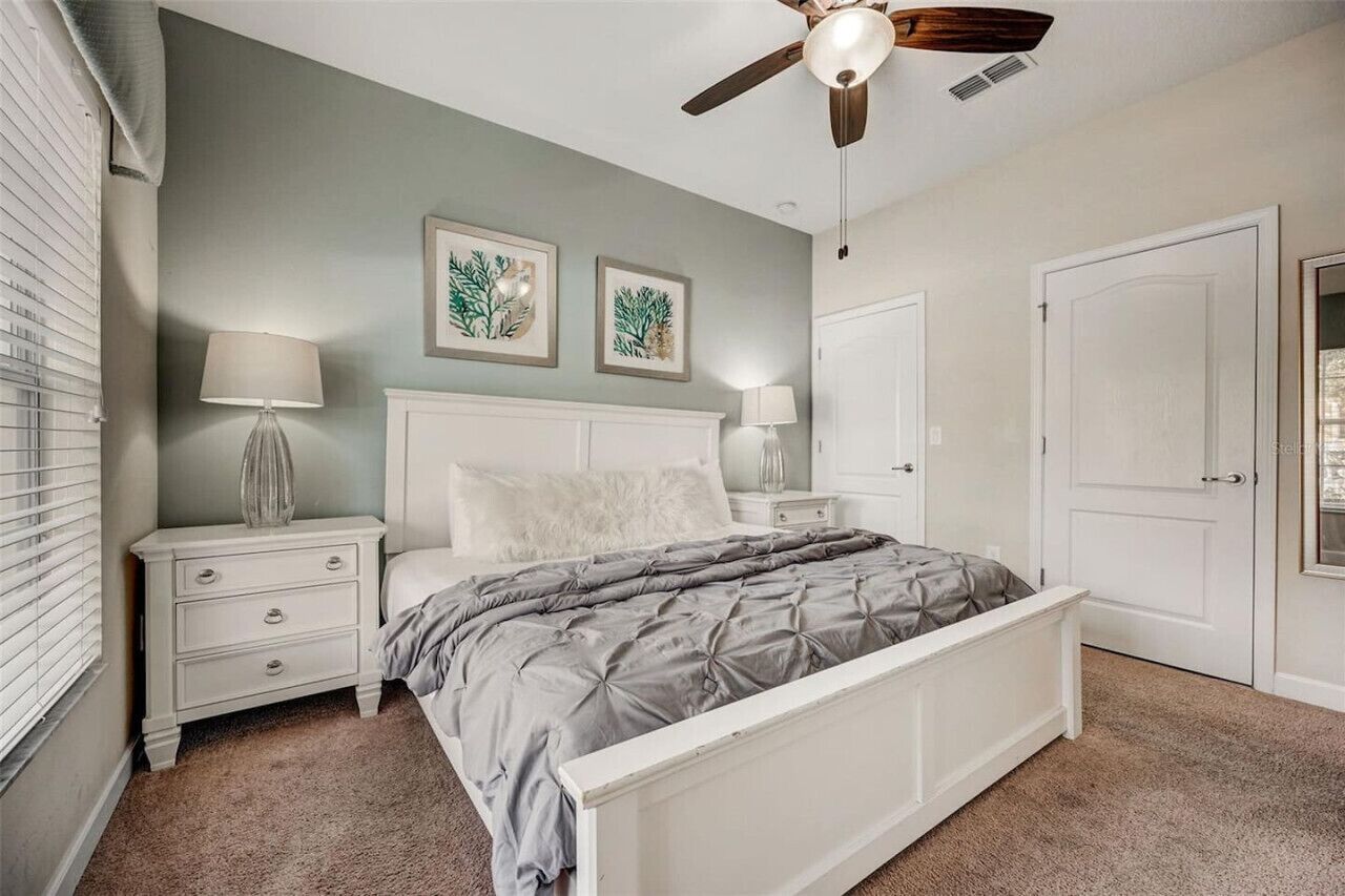 A bedroom with a bed, nightstands, a ceiling fan, and two framed pictures on the wall.