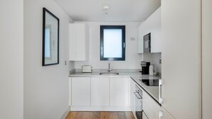 A compact kitchen with white cabinets, a built-in oven, a sink, and a window above the countertop. - Bright Aldgate 1BR, close to Train & Liverpool Street, by Blueground (London)