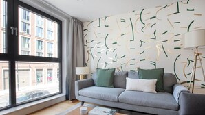 A modern living room with a grey sofa, a wooden coffee table, and a patterned wall. - Bright Aldgate 1BR, close to Train & Liverpool Street, by Blueground (London)