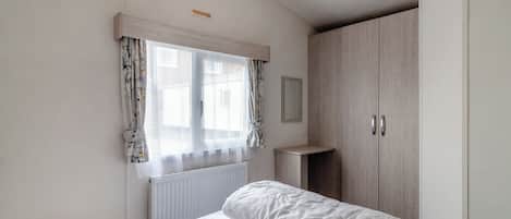 A bedroom with a bed, a window with curtains, a radiator, and a wardrobe.