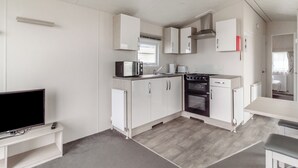 A compact kitchen with a microwave, toaster, and oven. There is a small dining area with a table and bench. - Castaways Oyster 10 (Pet) (Bacton-on-Sea)