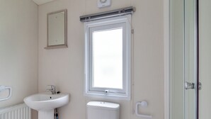 A bathroom with a toilet, a sink, a window, and a door. - Castaways Oyster 10 (Pet) (Bacton-on-Sea)