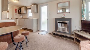 A compact living space with a kitchenette, a dining area, a seating area, and a fireplace. - Castaways Oyster 10 (Pet) (Bacton-on-Sea)