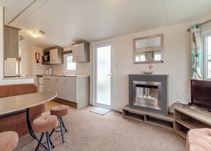 A compact living space with a kitchenette, a dining area, a seating area, and a fireplace. - Castaways Oyster 10 (Pet) (Bacton-on-Sea)