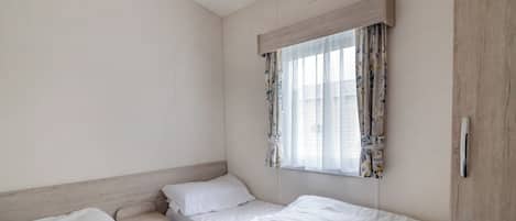 Habitación de hotel pequeña y sencilla con dos camas individuales, una ventana con cortinas florales y un cabecero de madera.