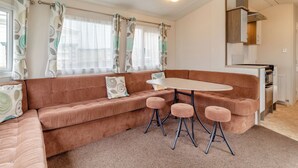 A cozy living area with a brown sofa, a small round table, and three matching stools. - Castaways Oyster 10 (Pet) (Bacton-on-Sea)