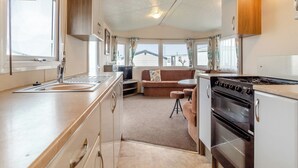 A compact RV kitchen with a stove, sink, and dining area. - Castaways Oyster 10 (Pet) (Bacton-on-Sea)