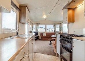 A compact RV kitchen with a stove, sink, and dining area. - Castaways Oyster 10 (Pet) (Bacton-on-Sea)