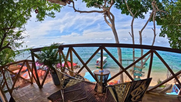 A beachside terrace with wooden flooring, wicker chairs, and a view of the ocean.