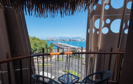 A balcony with two chairs and a table, overlooking a marina with boats and a distant mountain.