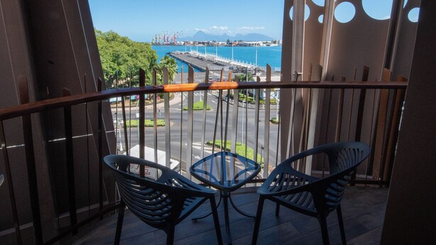 Un balcón con dos sillas y una mesa, con vista a un puerto deportivo con barcos y una montaña distante.