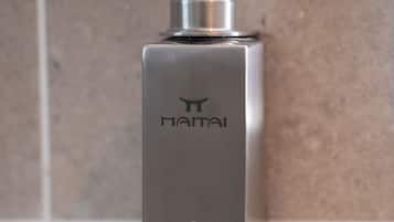 A metallic soap dispenser with a pump, labeled "Nai" and "SAVON SOAP," mounted on a tiled wall.