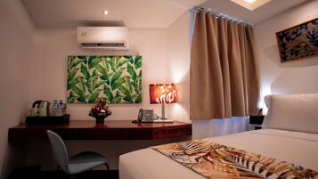 A hotel room with a bed, desk, chair, air conditioning unit, artwork, and curtains.