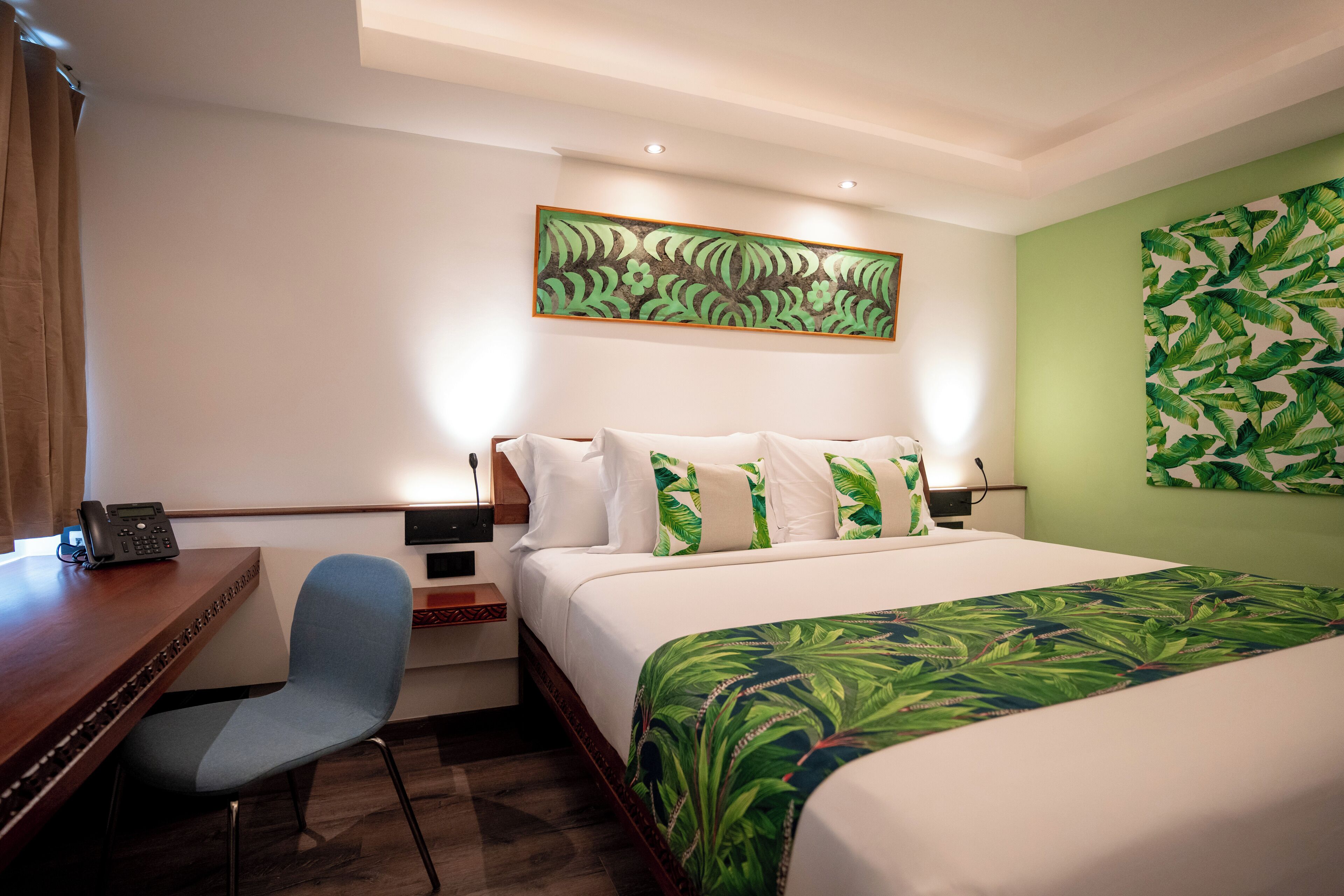 A hotel room with a bed, a desk, a chair, a telephone, and artwork on the walls.