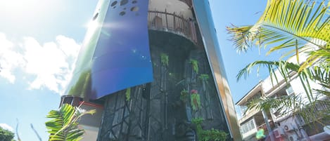 A tall, cylindrical building with a unique, perforated facade and a base adorned with greenery.