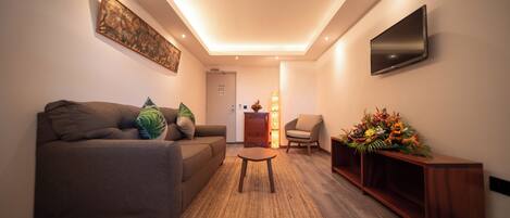 Un salon moderne avec un canapé, une petite table, un téléviseur fixé au mur et une composition florale décorative.