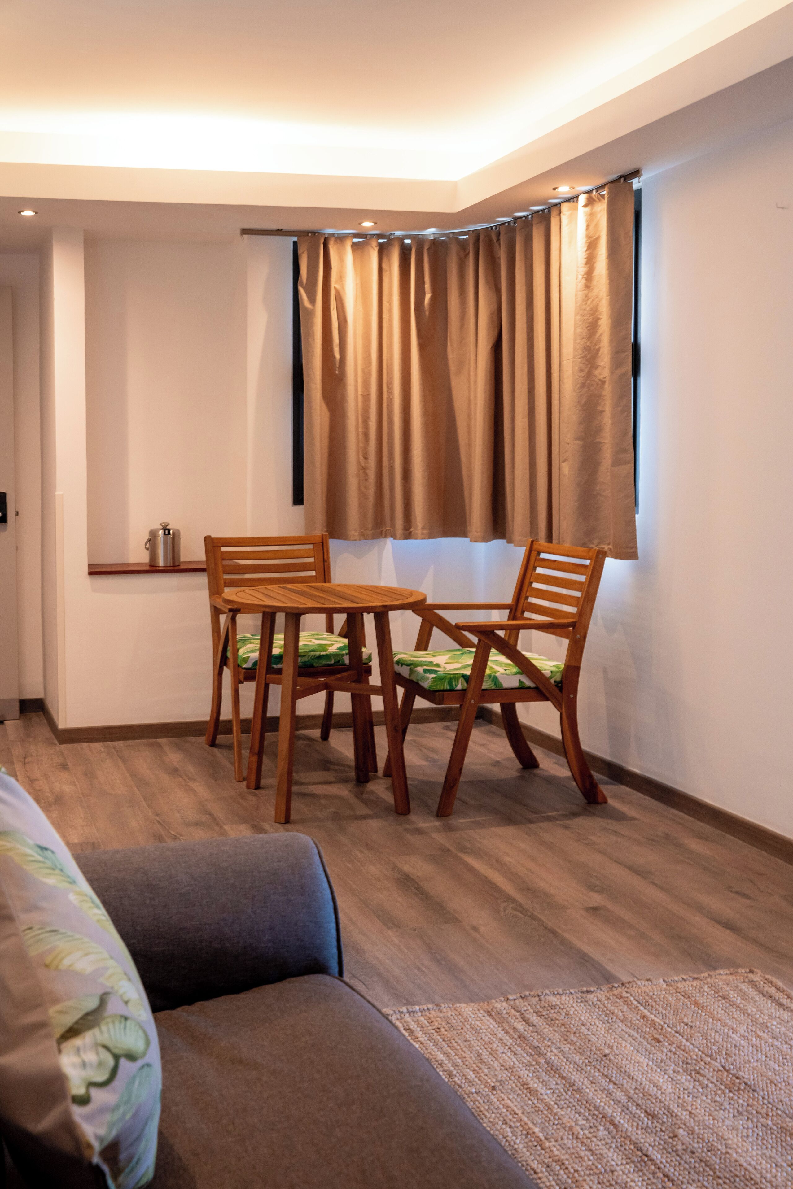 A small room with a wooden table and chairs, a sofa, and a window with curtains.