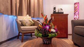 Un salón con una mesa de centro de madera, un arreglo floral, un sofá, un sillón, un mueble aparador y un aire acondicionado instalado en la pared.