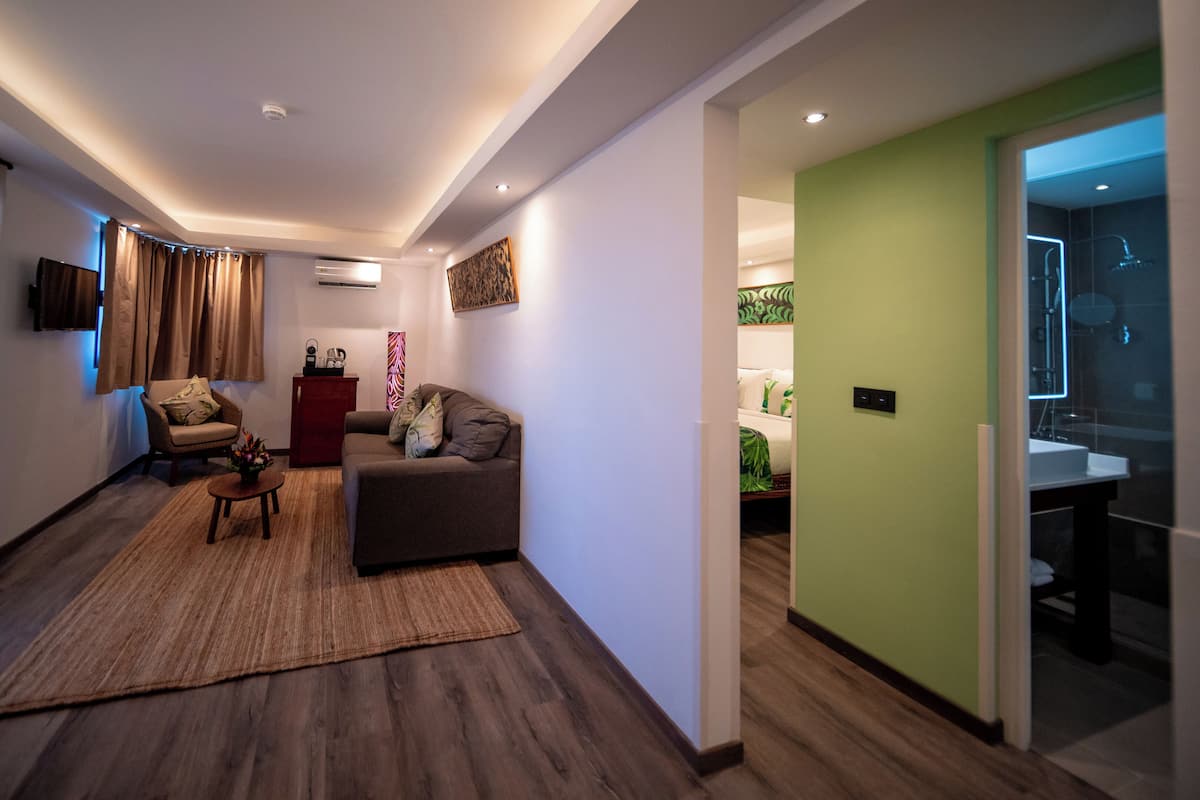 A modern living room with a sofa, a coffee table, and a TV. There is a wooden floor and a green wall.