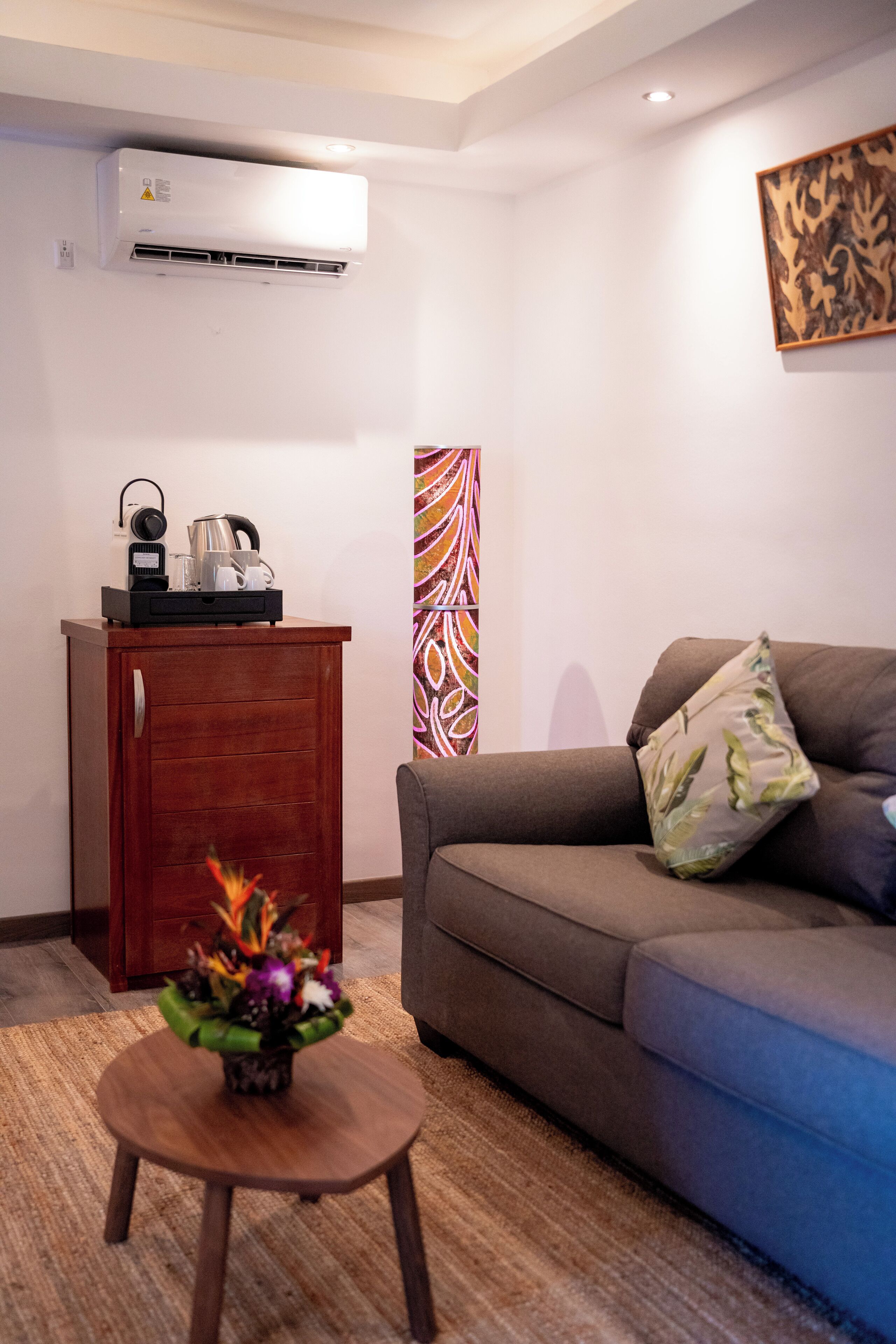 A living room with a brown sofa, a small wooden cabinet, and a coffee table with a floral arrangement.