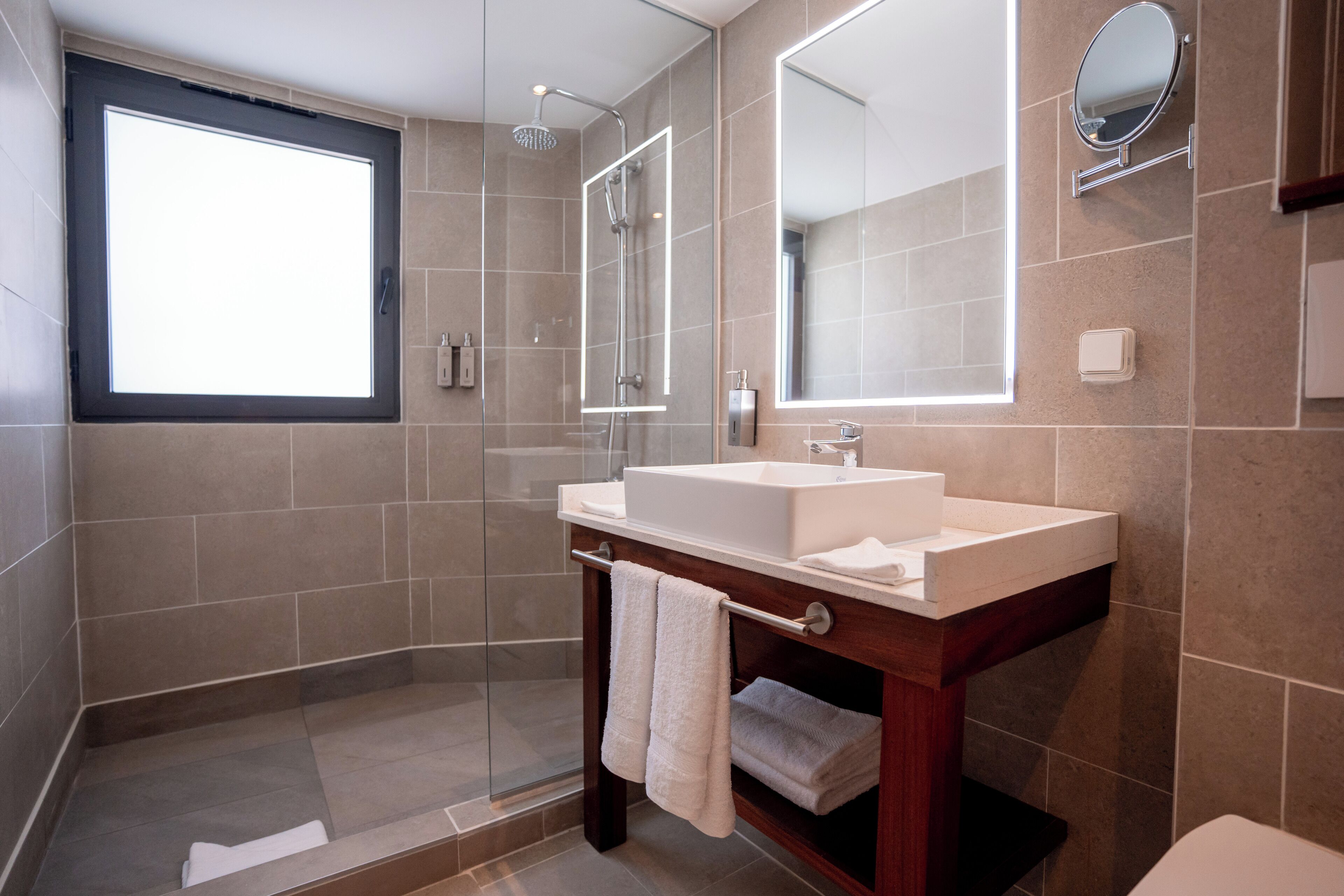 Une salle de bain moderne dotée d’une douche à parois de verre, d’un grand miroir et d’un meuble-lavabo avec un évier et un porte-serviettes.