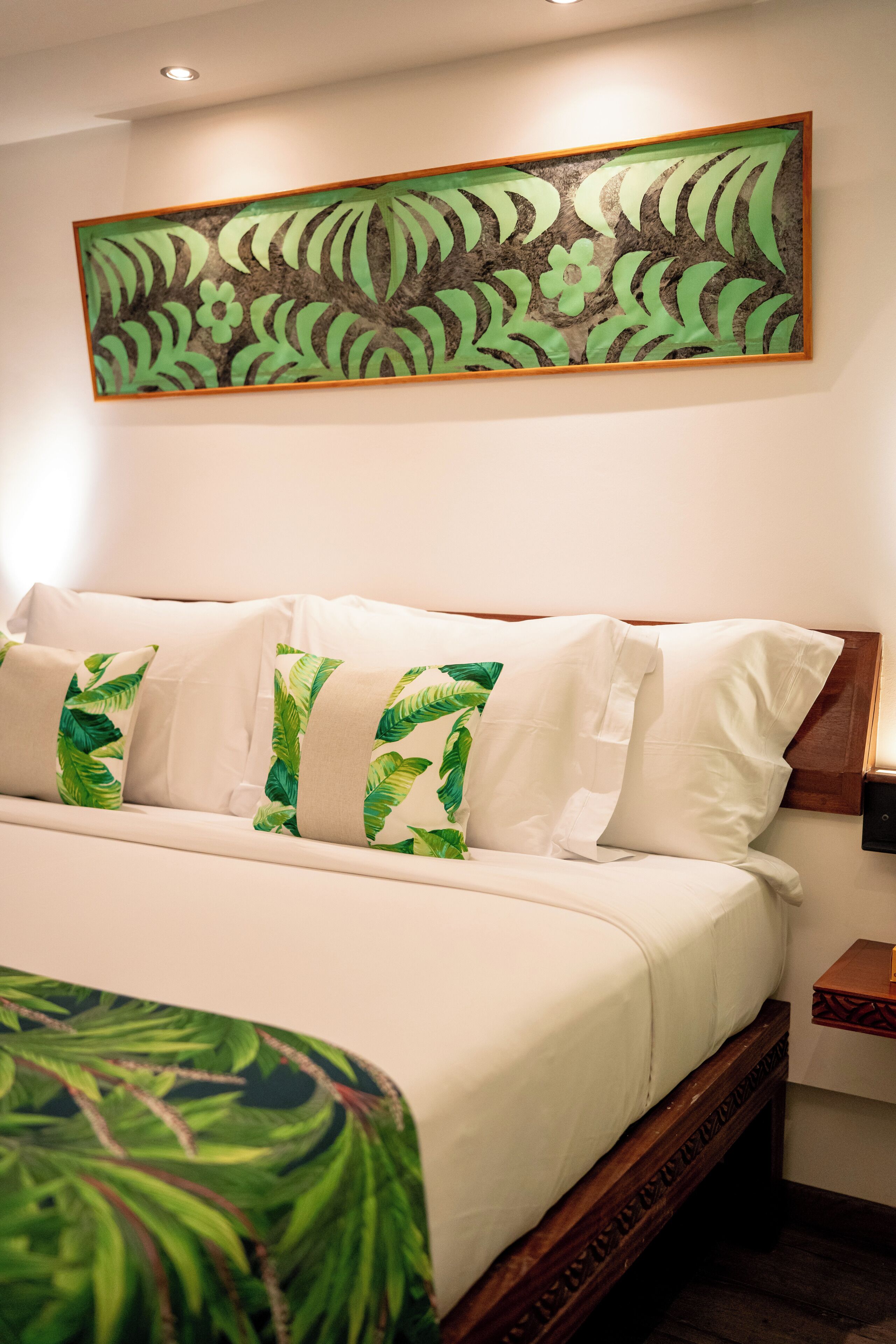 A hotel room with a bed, pillows, a nightstand, and a wall-mounted artwork.