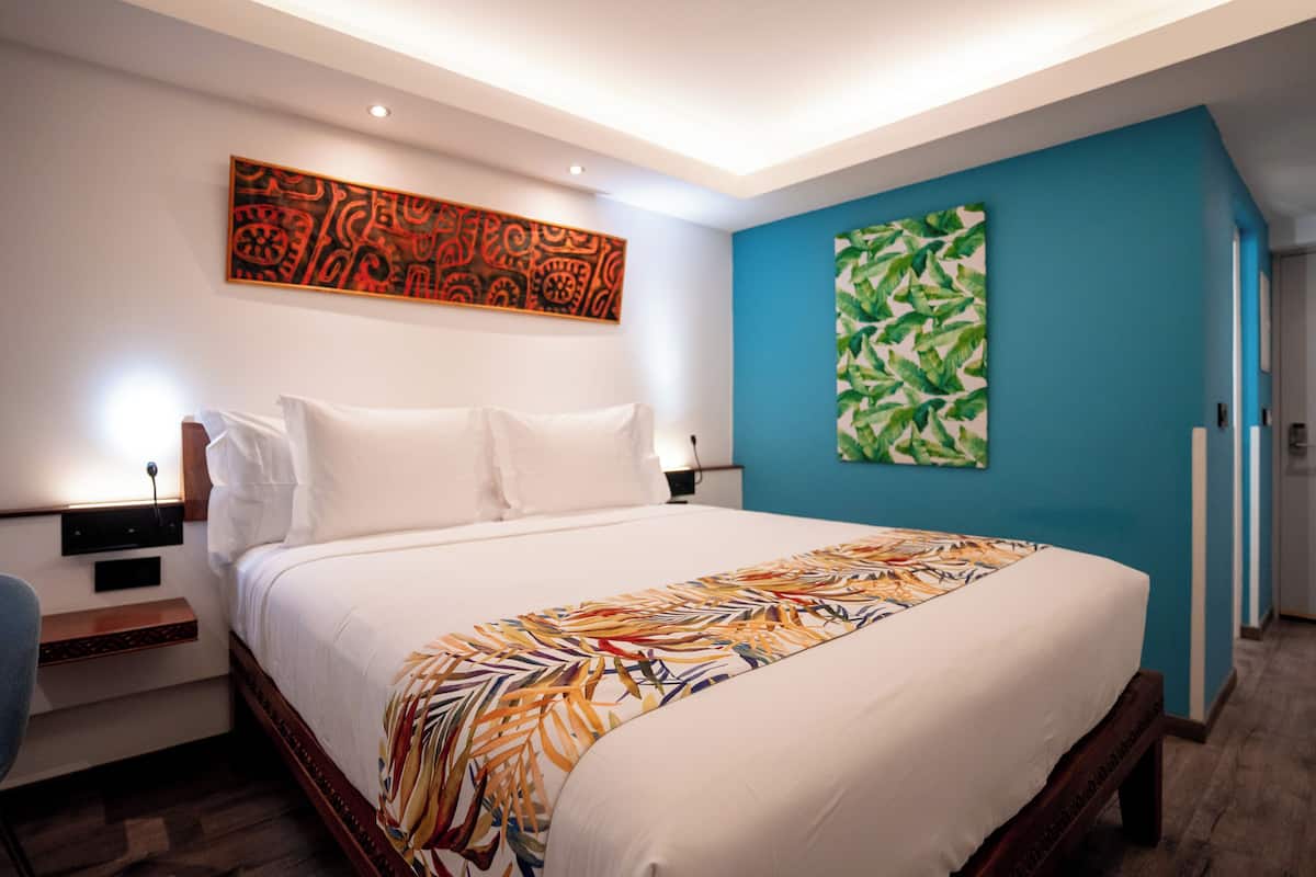 A modern hotel room with a large bed, a nightstand, a desk, and a chair.