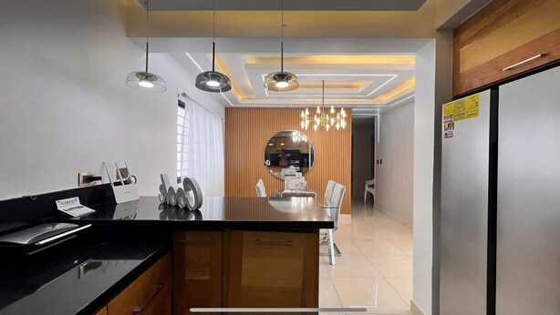 A modern kitchen with a central island, pendant lighting, and a view into the dining area.