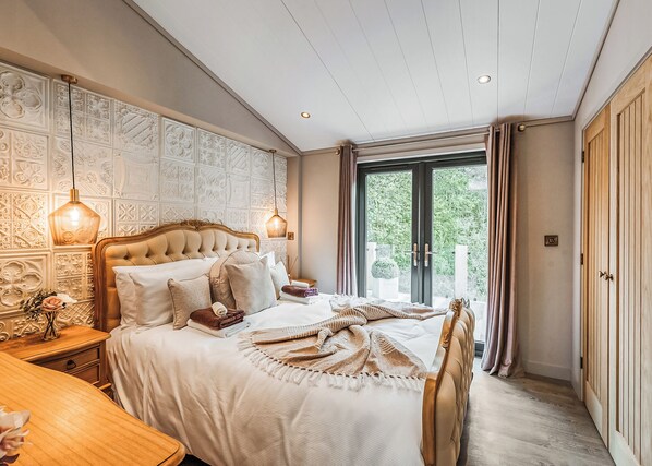 A bedroom with a large bed, a wooden nightstand, a bedside table, a decorative wall, and a view through a glass door.